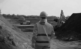 worker from behind dressed in work clothes observing some excavators on the construction site.